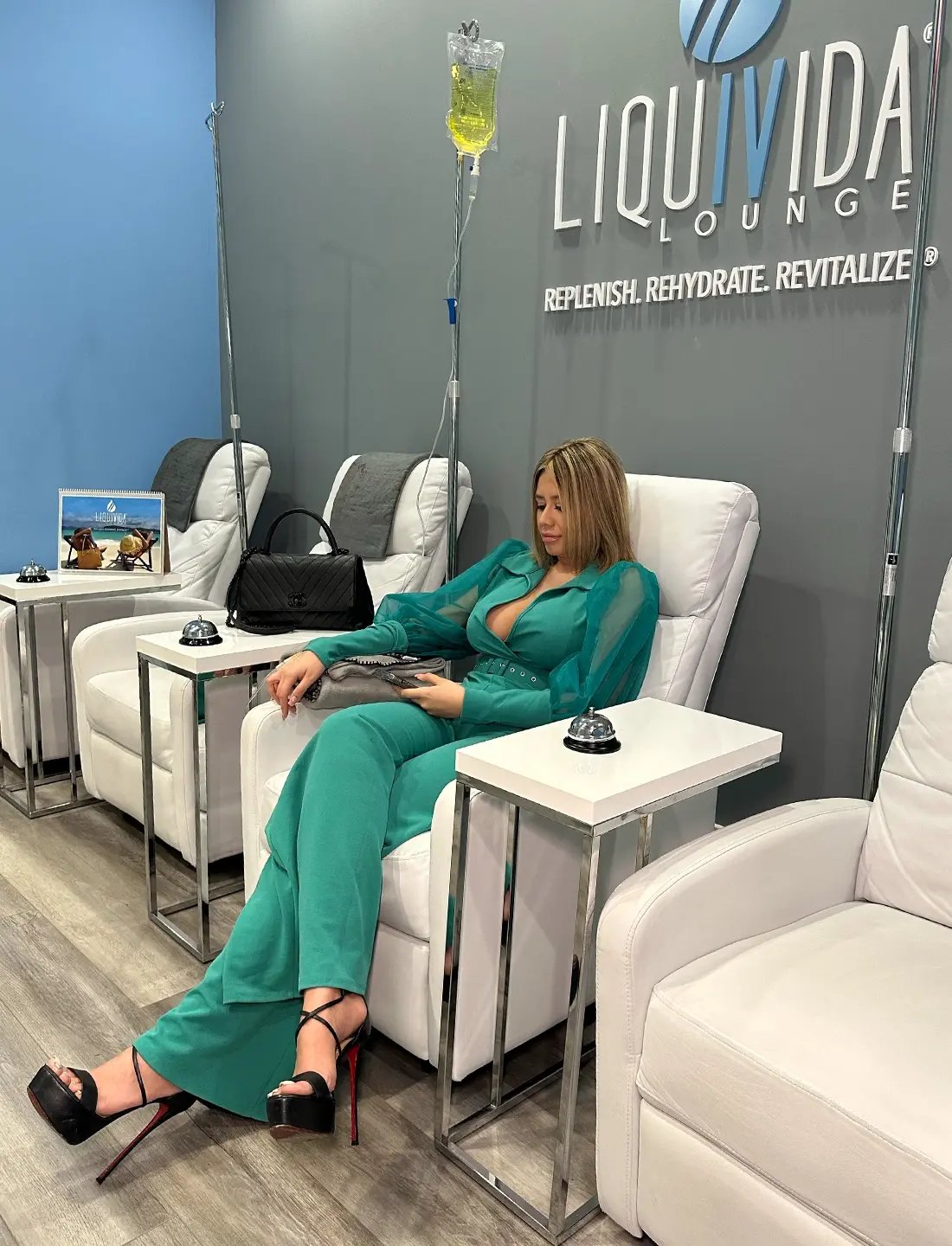 Woman wearing a teal suit sitting in a lounge getting an IV drip at Liquivida Wellness Center