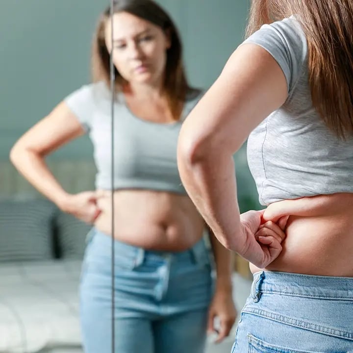 Woman looks at her belly in the mirror thinking about starting a Weight Loss program at Liquivida Wellness Center