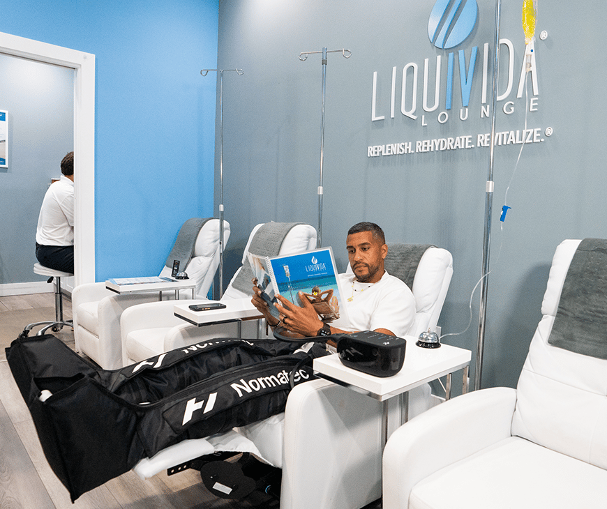 Man sitting in a chair at Liquivida Lounge wearing Normatec compression boots while getting an IV drip