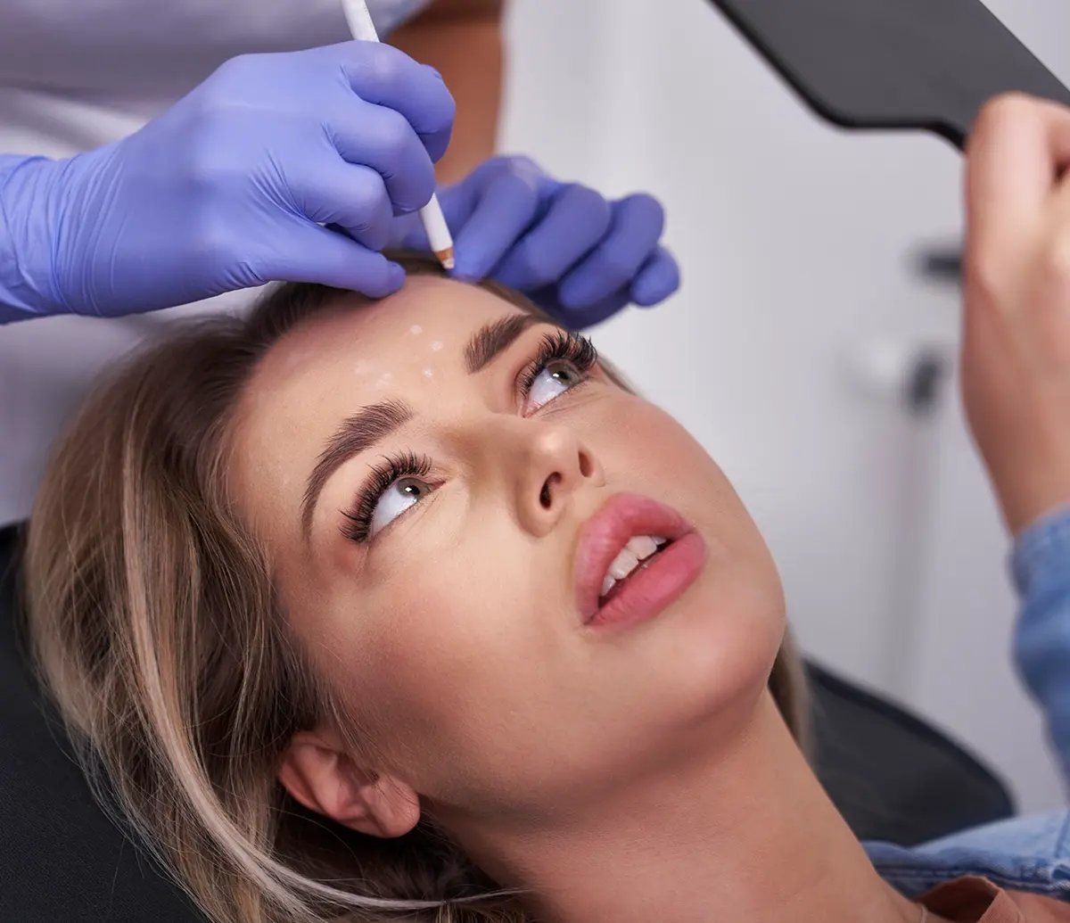 Woman looks at her face in a mirror while she waits for Sculptra treatment at Liquivida