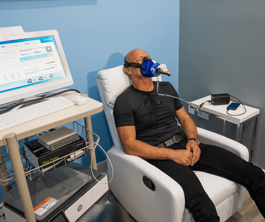 Jarek Tadla is sitting on a chair while a machine gathers his Resting Metabolic Rate data at Liquivida