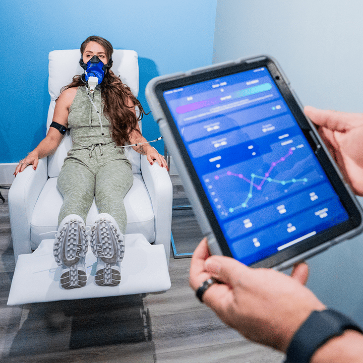 Melissa Lori sitting on a white chair while a device records her Resting Metabolic Rate data at Liquivida