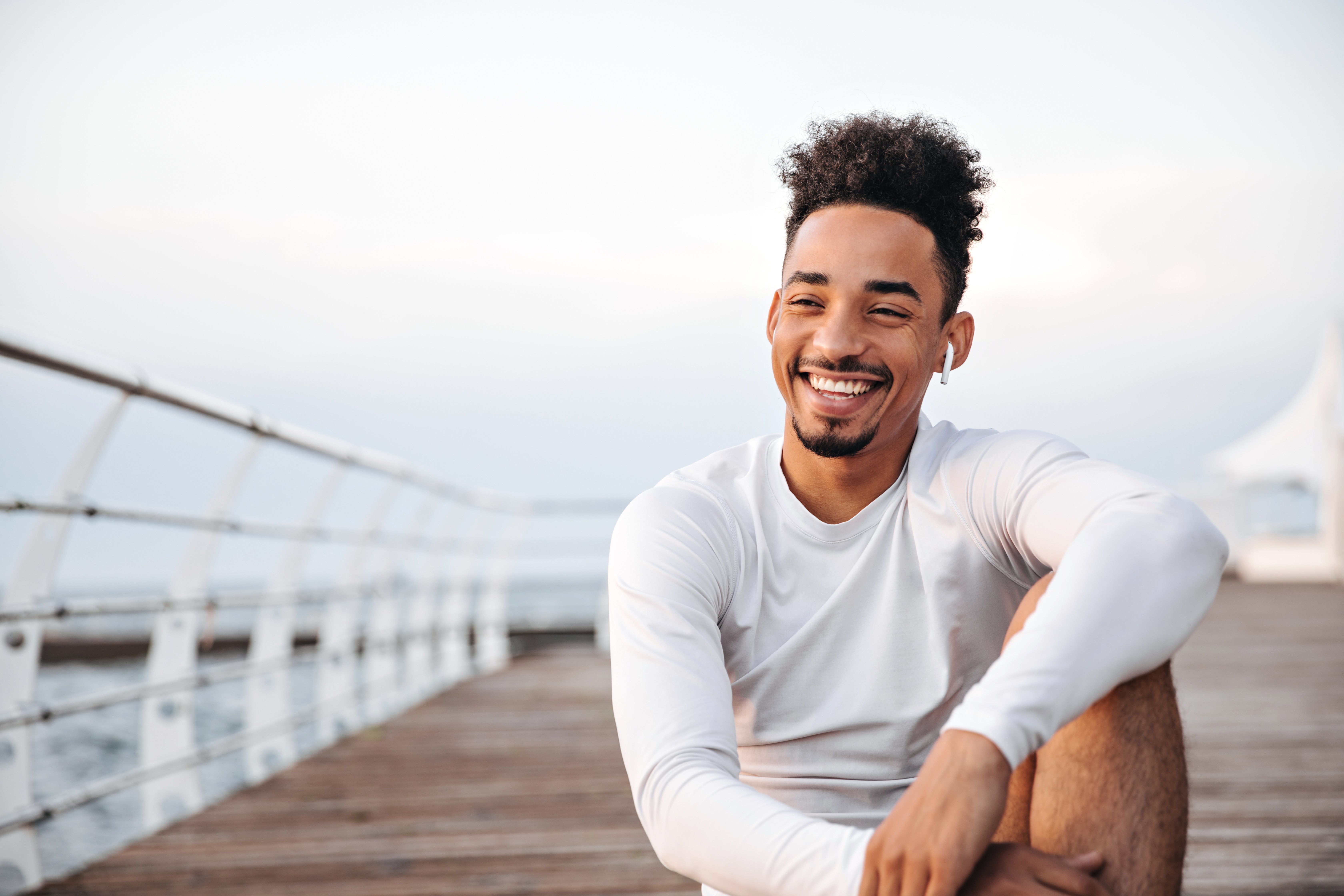 cheerful-curly-dark-skinned-man-white-long-sleeved-t-shirt-smiles-sincerely-rests-near-sea