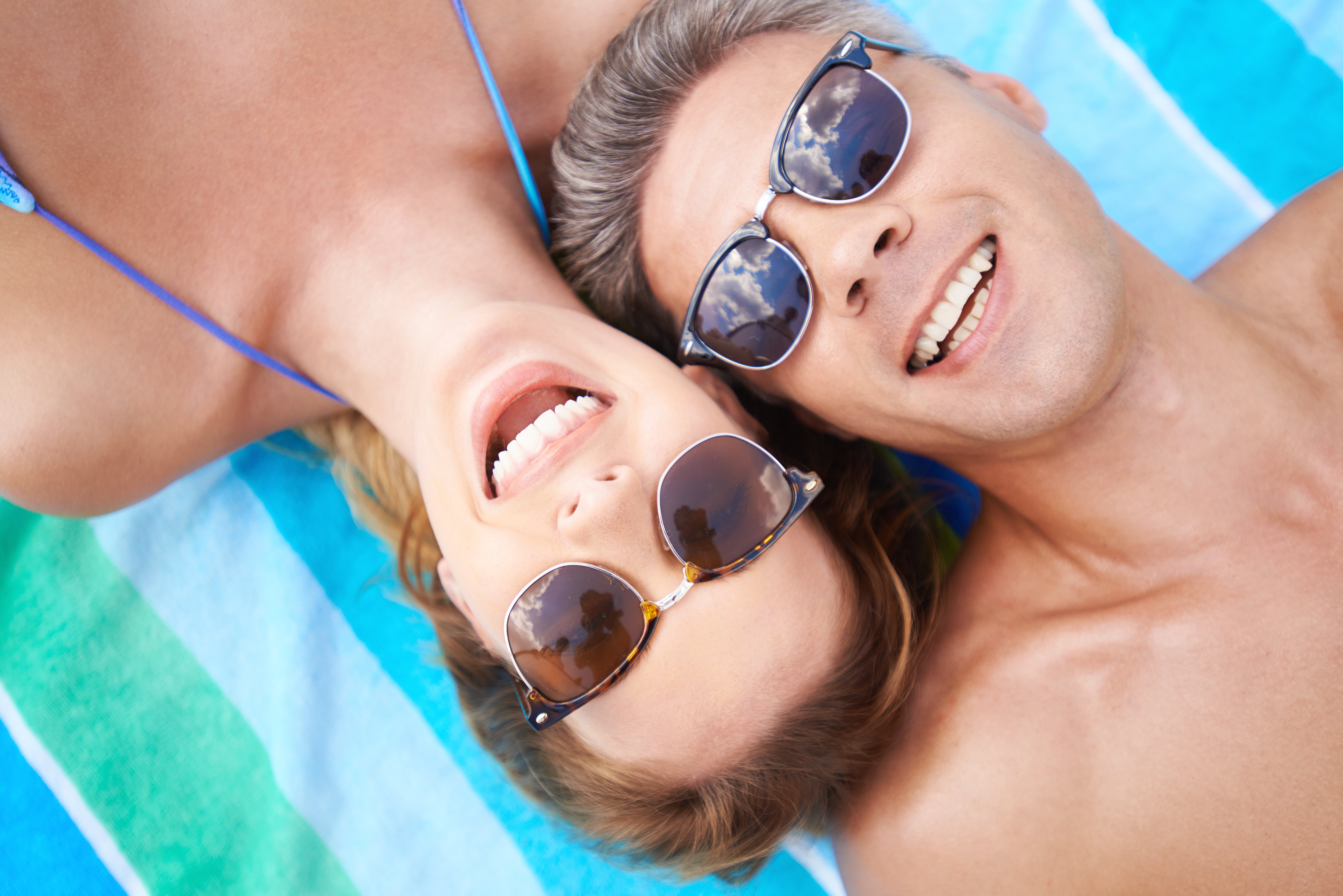 happy-couple-in-sunglasses-lying-on-the-beach-SBI-300730852