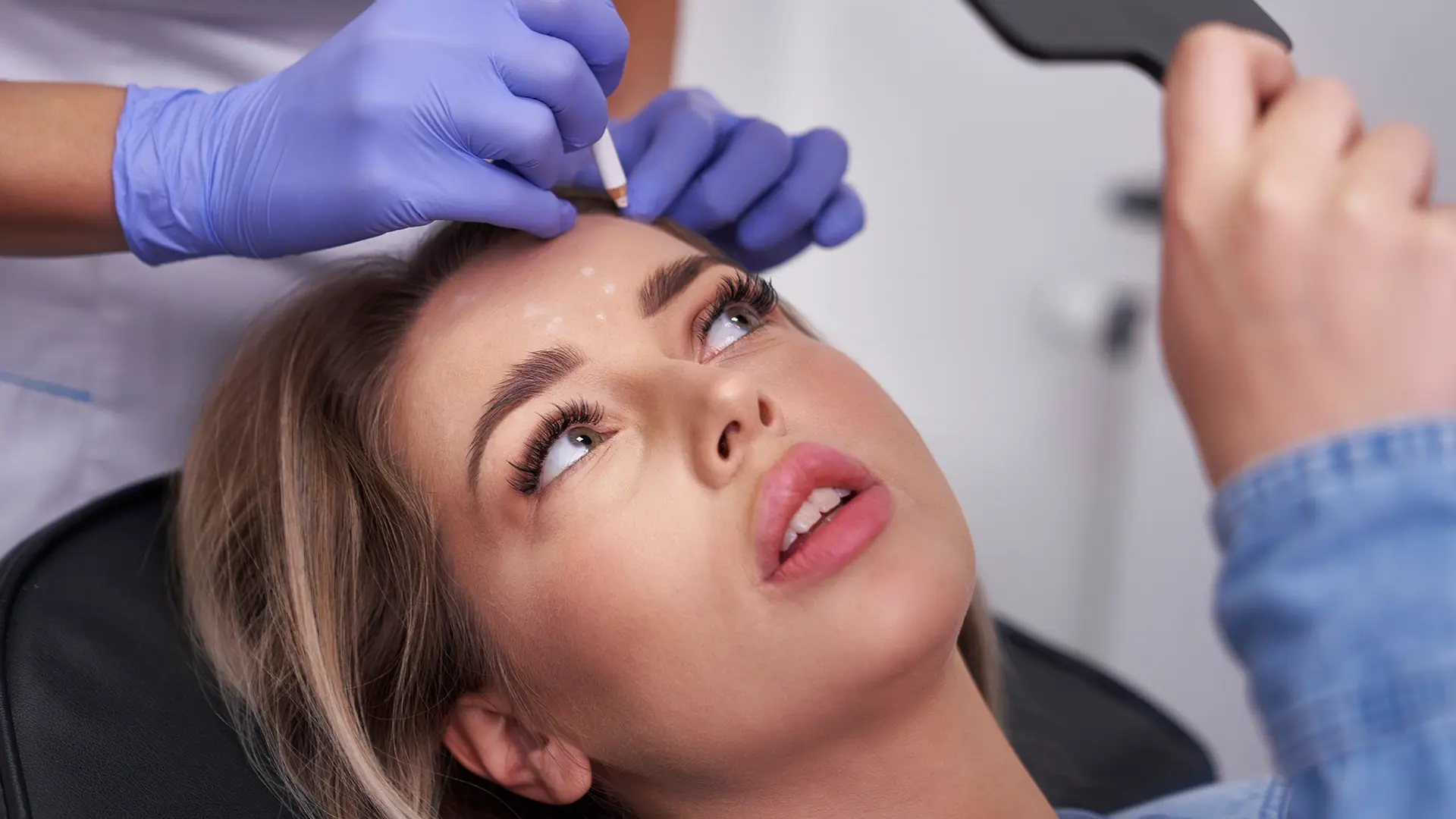 Woman looks at her face in a mirror while she waits for Sculptra treatment at Liquivida Wellness Center